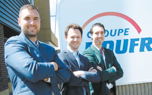 Three business professionals smiling in front of company sign.