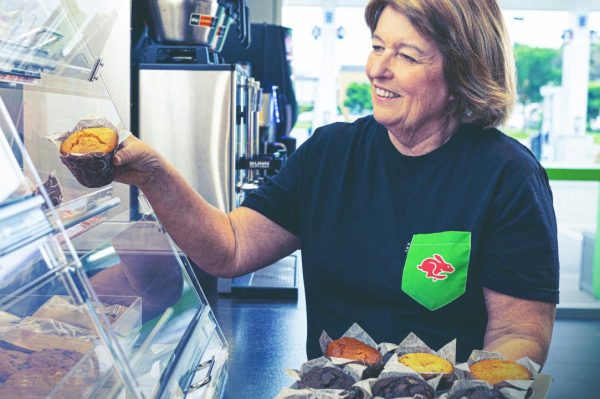Woman serving fresh muffins in a bakery.